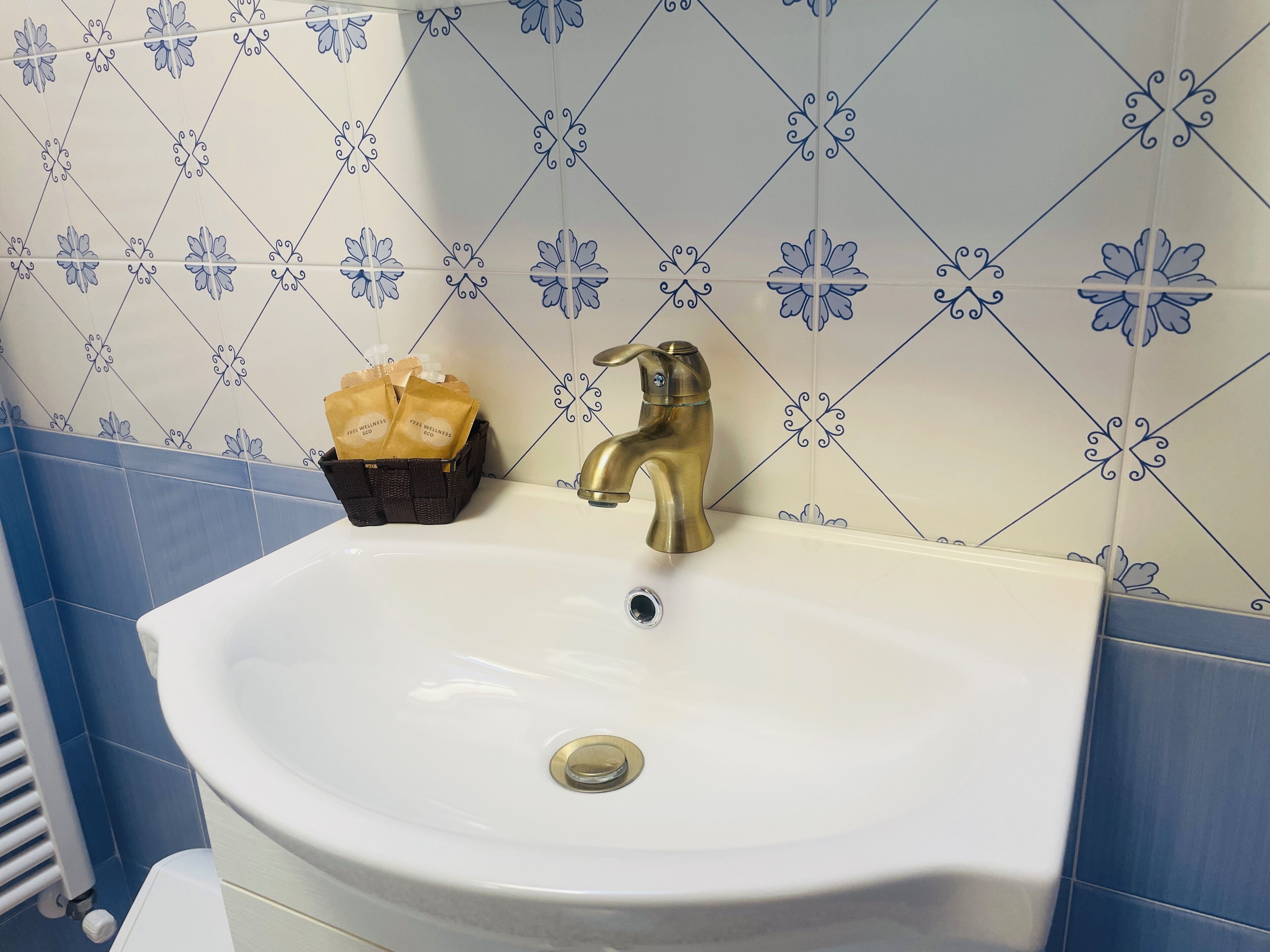 A bathroom with a white sink, a gold faucet, and a blue and white patterned wall. There is a basket with toiletries on the sink.