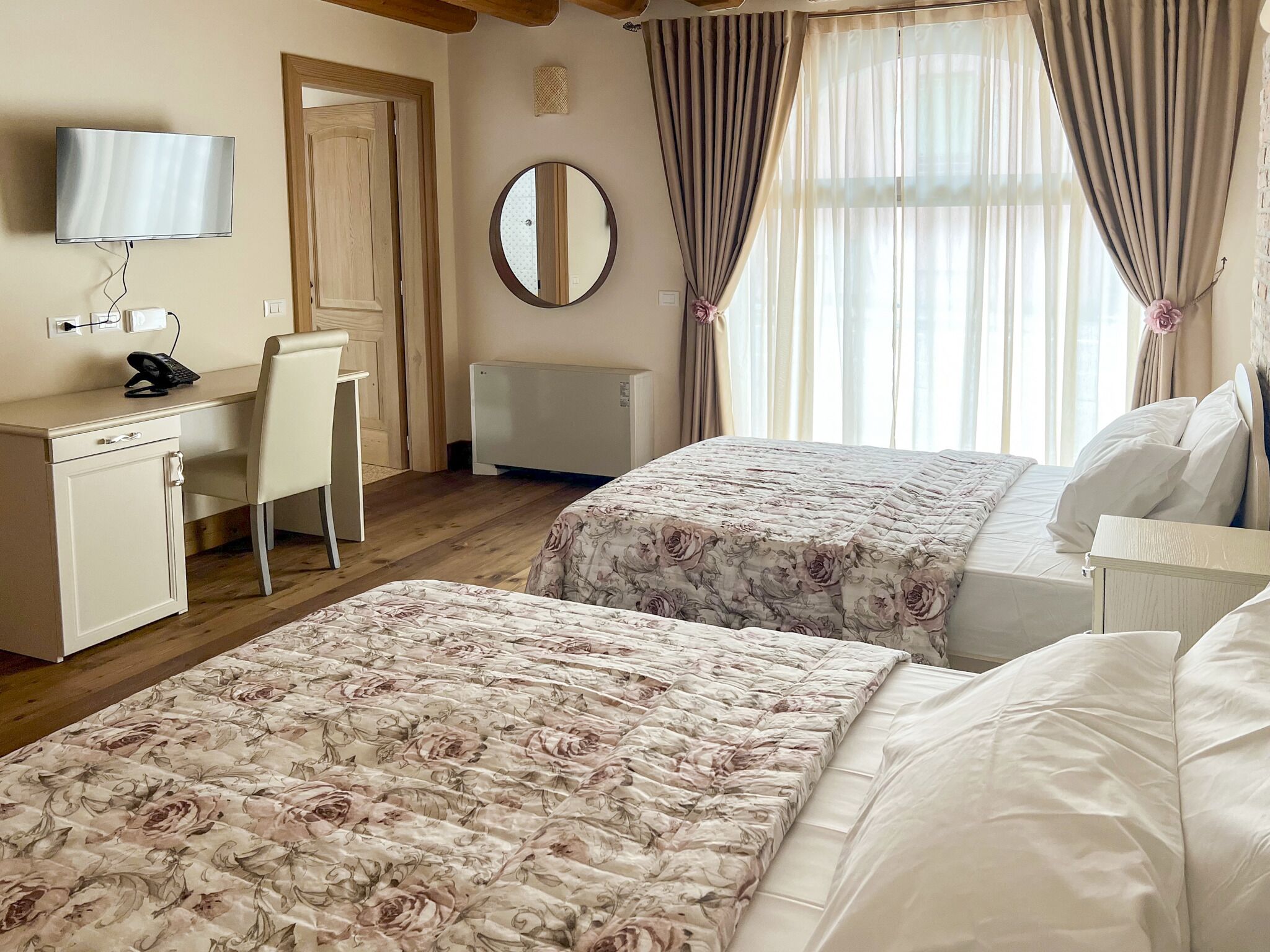 A hotel room with two beds, a desk, a chair, a television, and a mirror.