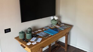 Een houten bureau met een vaas bloemen, een afstandsbediening en verschillende kaarten en brochures.
