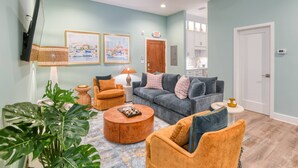 A living room with a sofa, armchairs, a coffee table, and a TV mounted on the wall.