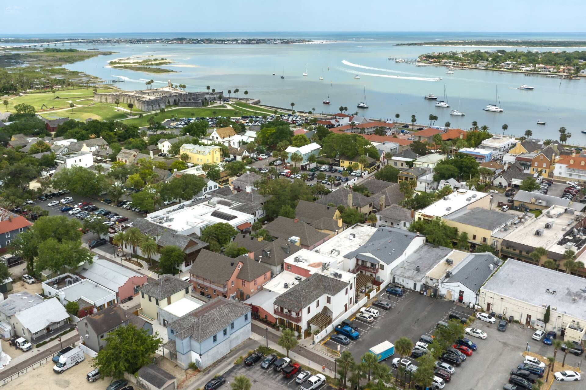 An aerial view of a coastal town with a marina, historic buildings, and a large parking area.