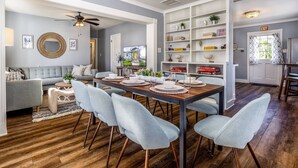 A dining area with a wooden table, light blue chairs, and a white shelving unit with books and decorative items. - Saragossa Sunshine (St. Augustine)