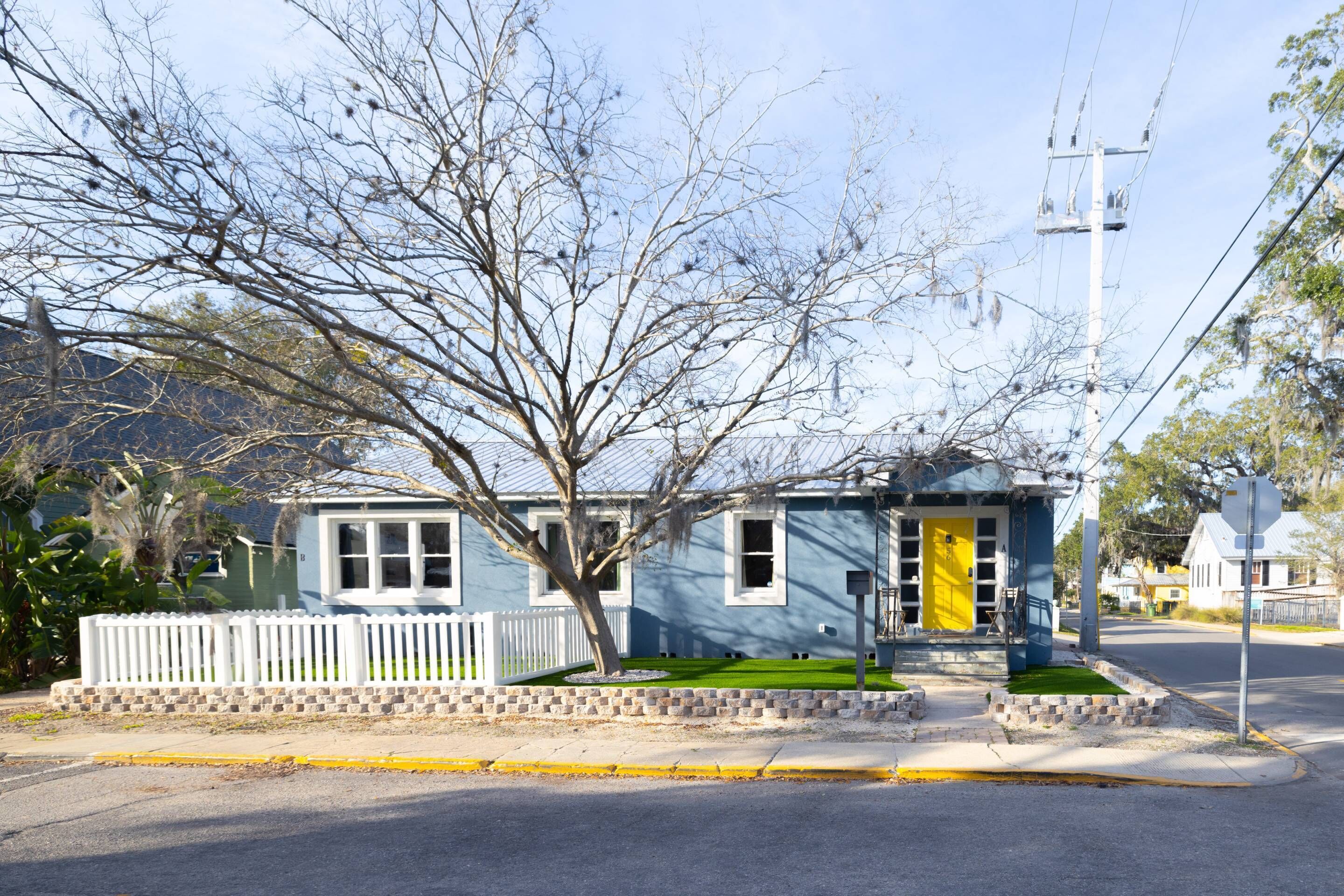 A two-story house with a white picket fence, a tree in front, and a yellow door.