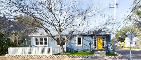 A two-story house with a white picket fence, a tree in front, and a yellow door.