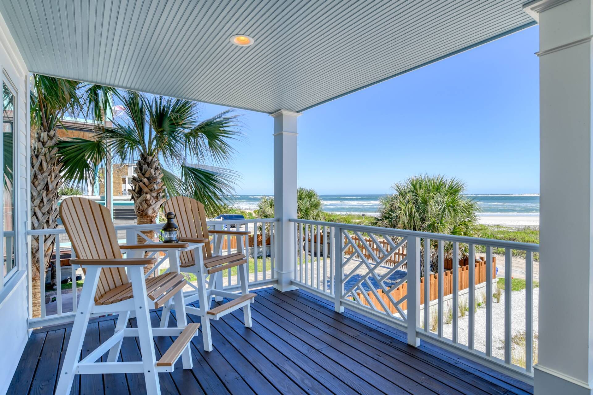A covered outdoor area with wooden chairs and a table, overlooking a beach.