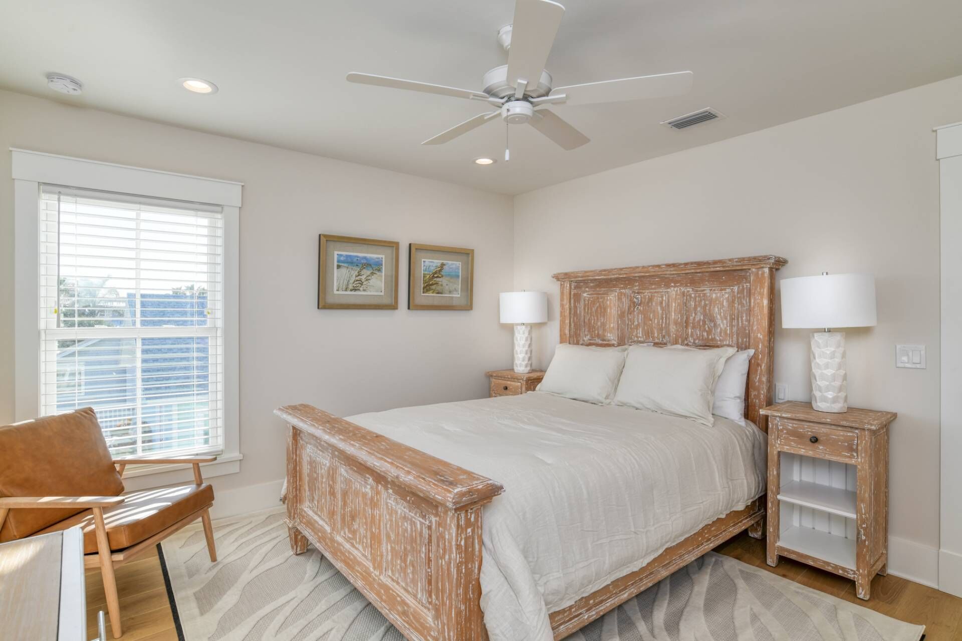 A bedroom with a large bed, two bedside tables with lamps, a ceiling fan, and a window with blinds.