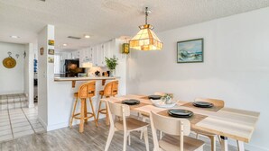 A modern kitchen with white cabinets, a wooden dining table with four chairs, and a hanging pendant light. - Pier Point 17 (St. Augustine)