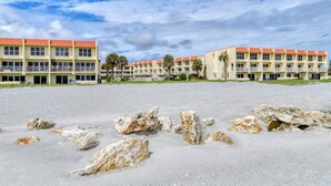 A beachfront hotel with multiple-story buildings, a sandy foreground with scattered rocks, and a clear sky. - Pier Point 17 (St. Augustine)