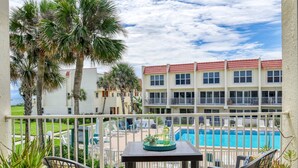 A balcony with a table and chairs, overlooking a swimming pool and a building with red roofs. - Pier Point 17 (St. Augustine)