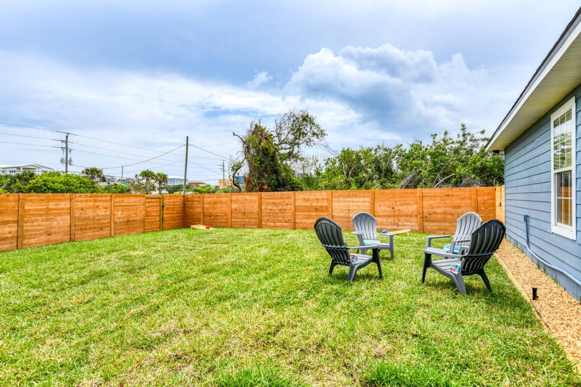 Un jardin avec une clôture en bois, une pelouse verdoyante et deux fauteuils Adirondack.