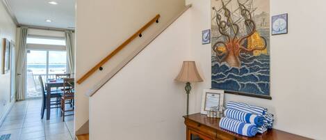 Eine Treppe mit Holzgeländer, ein Essbereich mit Tisch und Stühlen sowie eine Wand mit Wandteppich und einem Schrank mit Handtüchern.