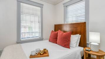 Una camera da letto ordinata con un letto, cuscini, un vassoio con tazze e una brocca, e un comodino con una lampada e un telefono.