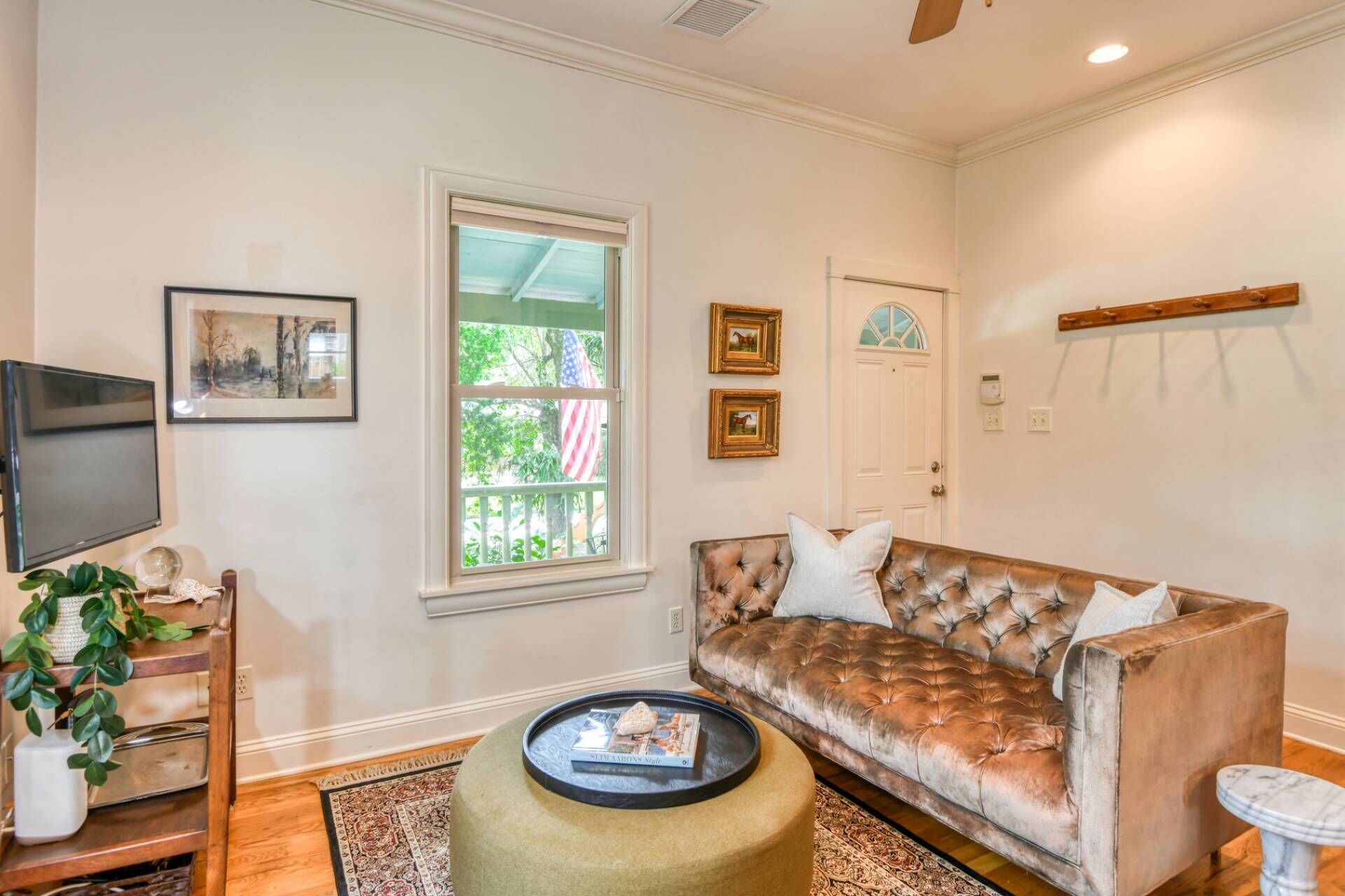 A living room with a sofa, a coffee table, a TV, and a window with an American flag.
