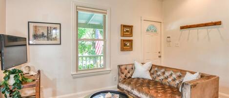 A living room with a sofa, a coffee table, a TV, and a window with an American flag.
