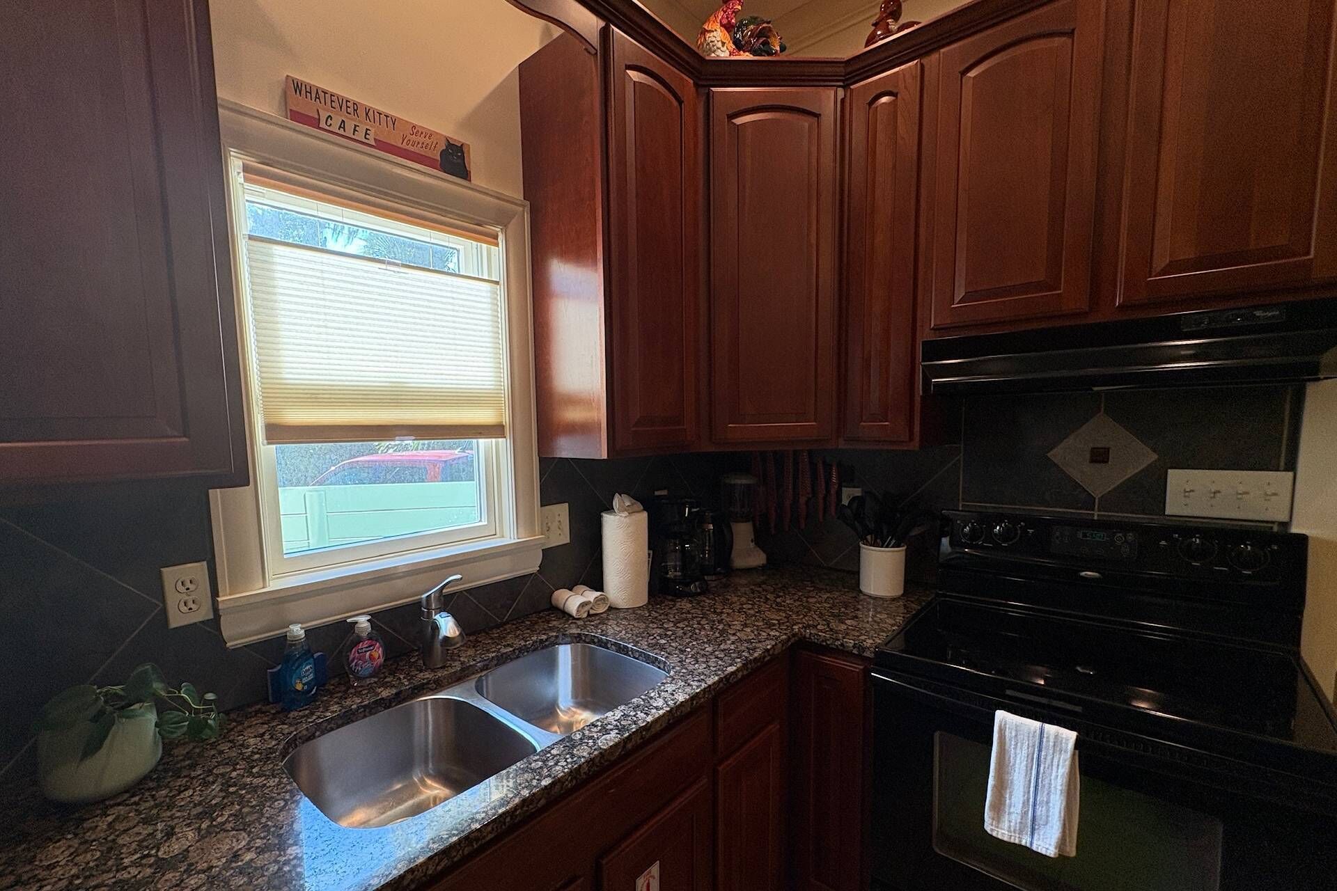 A kitchen with wooden cabinets, a stainless steel sink, a stove, and a window with blinds.