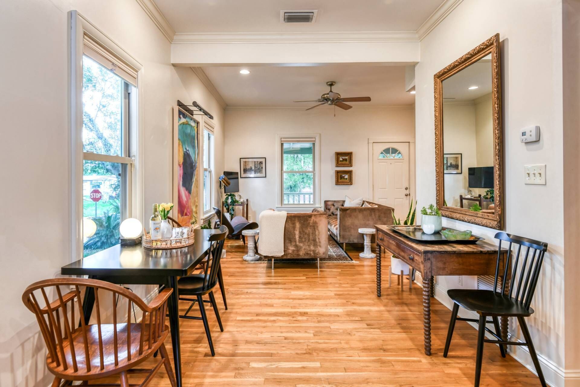 Quarto amplo com piso de madeira, mesa de jantar com cadeiras, sofá, espelho grande e ventilador de teto.