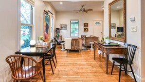 A spacious room with hardwood flooring, a dining table with chairs, a sofa, a large mirror, and a ceiling fan. - Little Blue Cottage (St. Augustine)