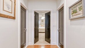 Un pasillo con suelo de madera que conduce a un dormitorio con cama y ventilador de techo.