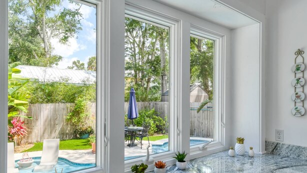 Una habitación amplia con ventanas grandes, una encimera de mármol y vista a un patio trasero con piscina y mobiliario de jardín.