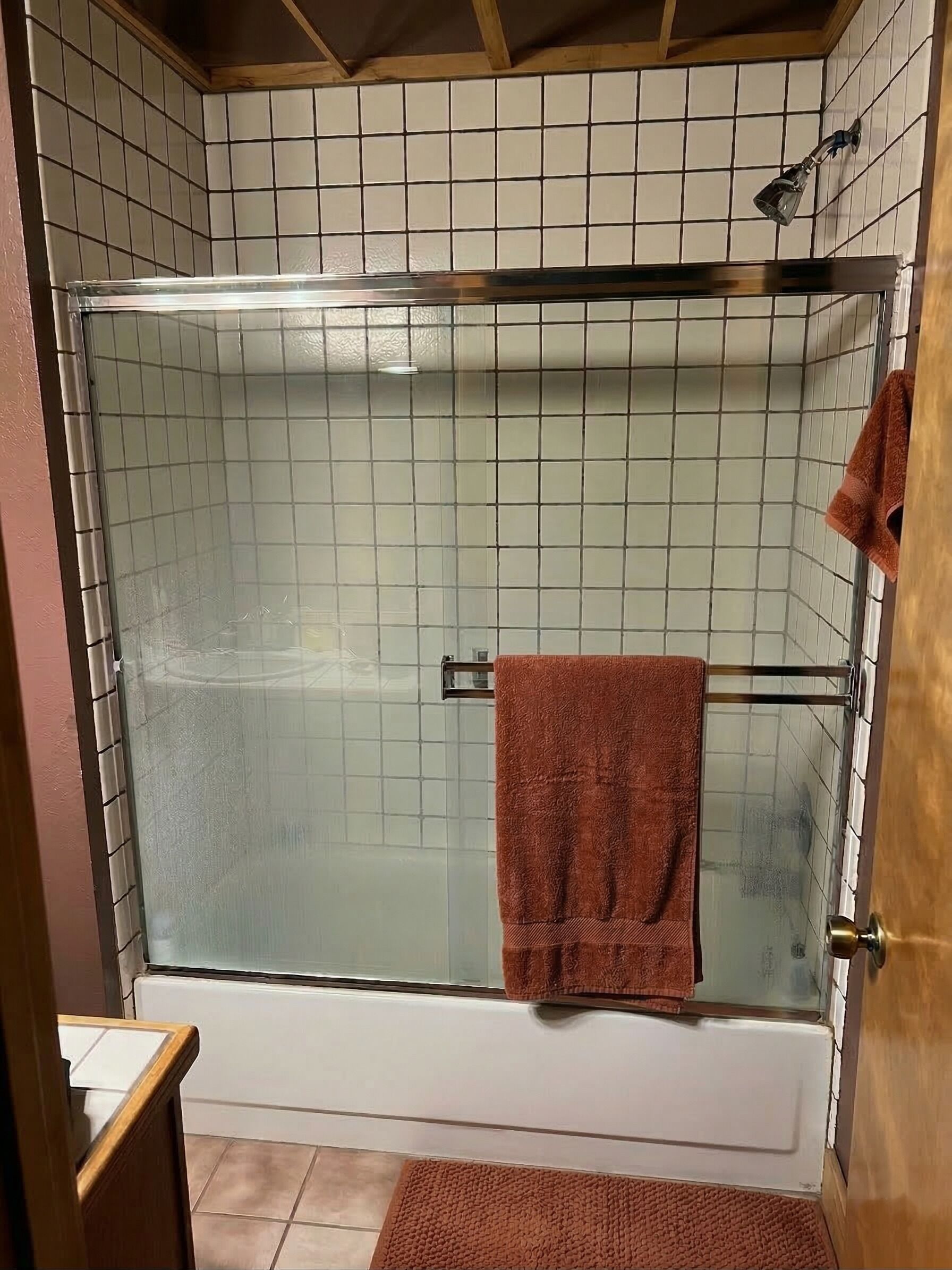 A glass-enclosed shower with a towel rack, a wooden door, and a tiled wall.
