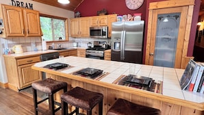 A modern kitchen with wooden cabinets, a stainless steel refrigerator, and a central island with stools. - Truckee Mountain Retreat + Trails + Pet Friendly (Truckee)