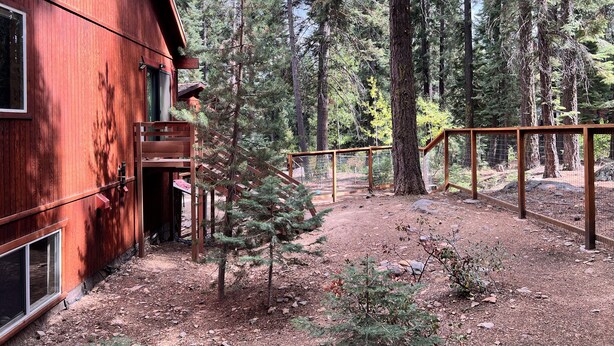 A wooden cabin with a balcony and a fenced deck area surrounded by tall pine trees. - Truckee Mountain Retreat + Trails + Pet Friendly (Truckee)