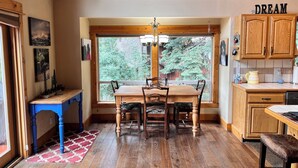 A dining area with a wooden table and chairs, a window with a view of trees, and wooden cabinets with a 'DREAM' sign. - Truckee Mountain Retreat + Trails + Pet Friendly (Truckee)