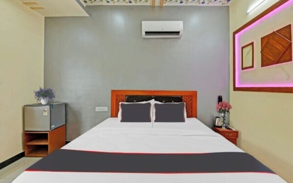 Habitación de hotel con cama, unidad de aire acondicionado, mesita de noche y estante en la pared.