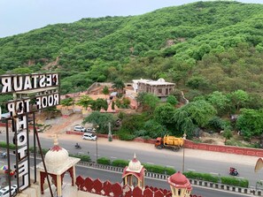 A hotel with a signboard, a road with vehicles, and a green hill in the background.