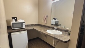 A compact bathroom with a sink, mirror, and a compact refrigerator. - The Sawmill Inn (Houston)