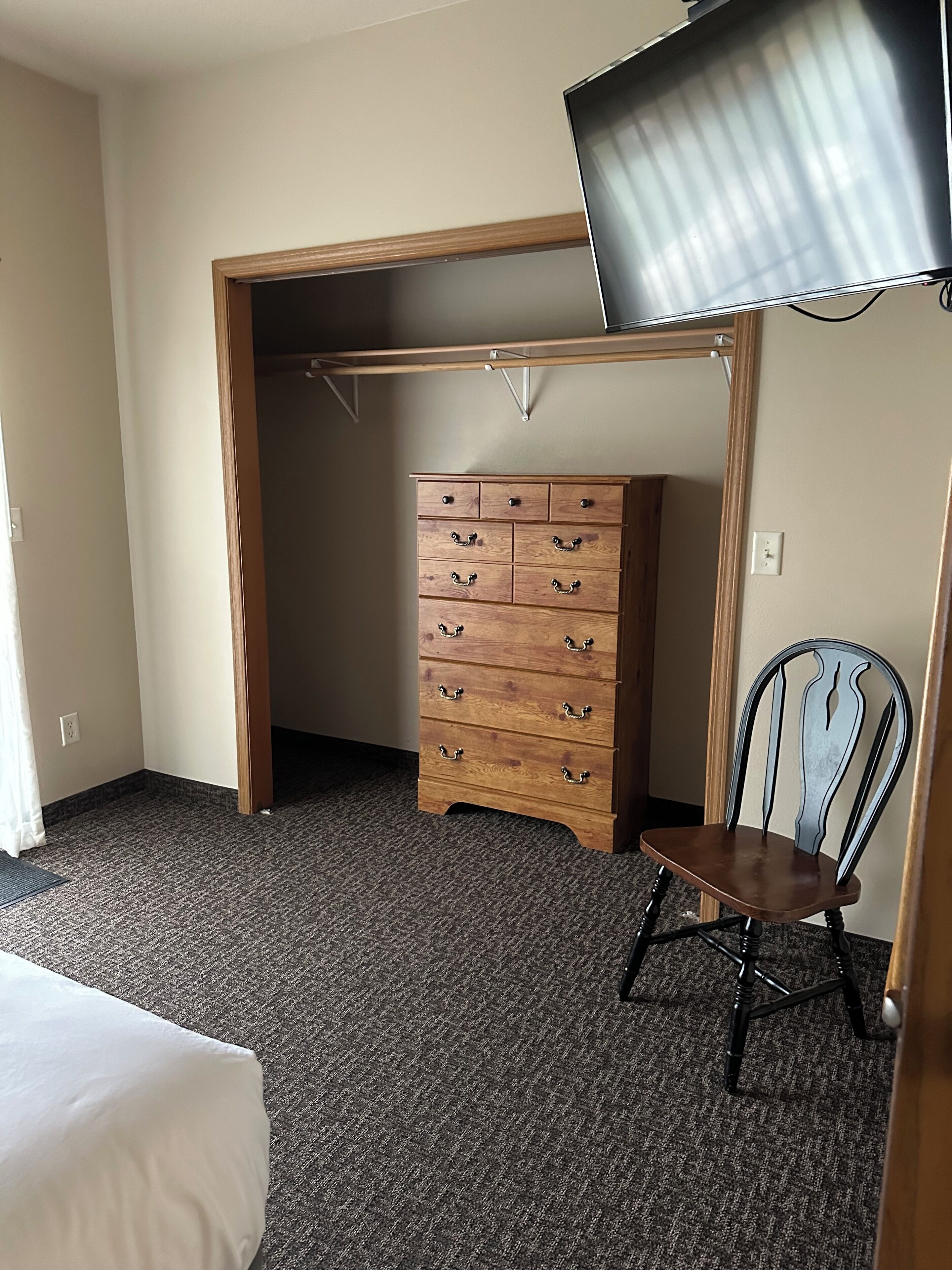 A bedroom with a bed, a wooden dresser, a chair, and a television mounted on the wall.