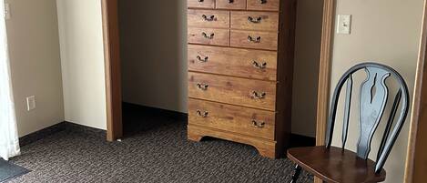 A bedroom with a bed, a wooden dresser, a chair, and a television mounted on the wall.