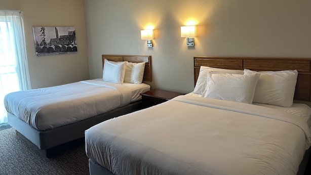 A hotel room with two beds, a nightstand, and two wall-mounted lamps. - The Sawmill Inn (Houston)