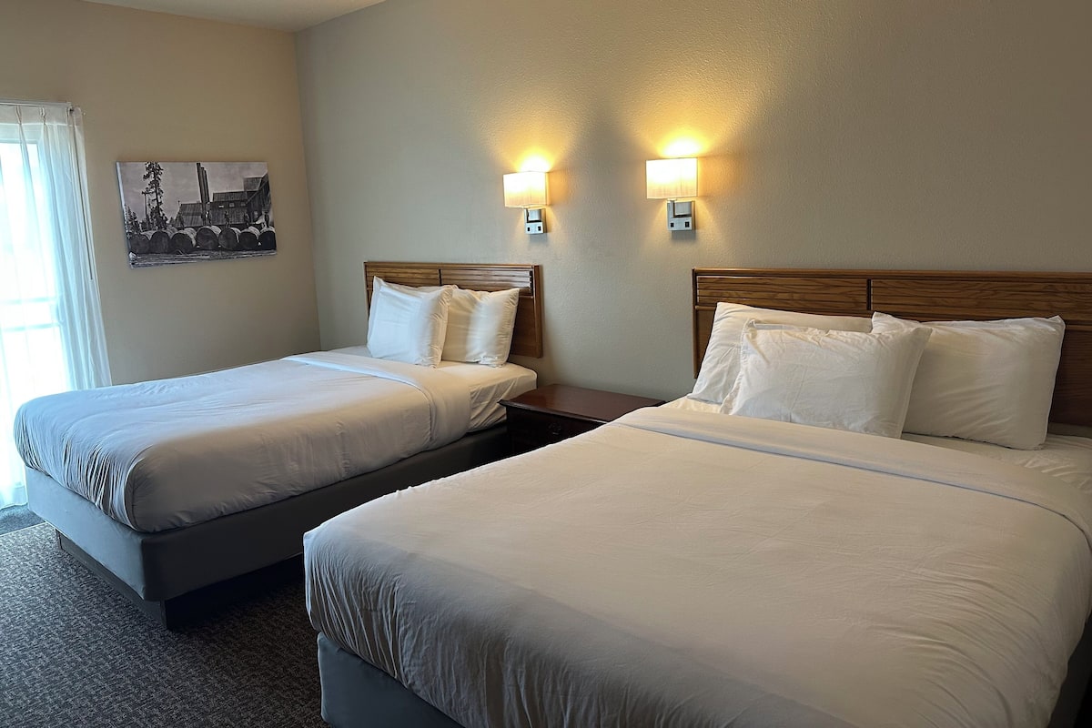 A hotel room with two beds, a nightstand, and two wall-mounted lamps.