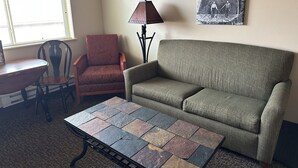 A living room with a green sofa, a red armchair, a wooden table, and a floor lamp. - The Sawmill Inn (Houston)