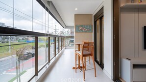 A modern balcony with a view of a city street, a dining table with chairs, and a mounted menu. - Apart w/ 2 Suites in Jurere Internacional Vvc0202 (Florianópolis)