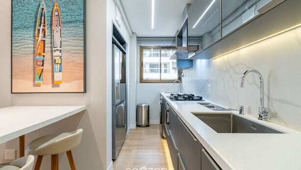 A modern kitchen with a long countertop, stainless steel appliances, and a window providing natural light. - Apart w/ 2 Suites in Jurere Internacional Vvc0202 (Florianópolis)