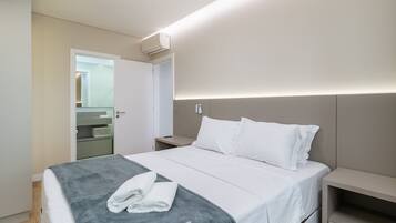 A modern hotel room with a neatly made bed, a bedside table, and a built-in shelf.