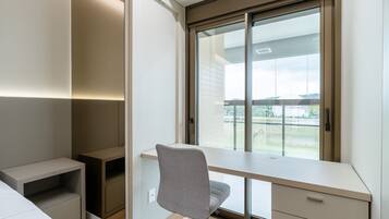 A modern bedroom with a built-in desk, a chair, and a large window offering a view of the outdoors.