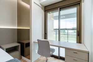 Un dormitorio moderno con escritorio empotrado, una silla y un amplio ventanal con vistas al exterior.