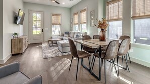 Un comedor amplio con una mesa y sillas de madera, un ventilador de techo y ventanas grandes con persianas.