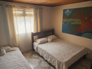 A bedroom with a bed, a smaller bed, and a window with curtains. - Monteverde Monkey Hostel (Monteverde)