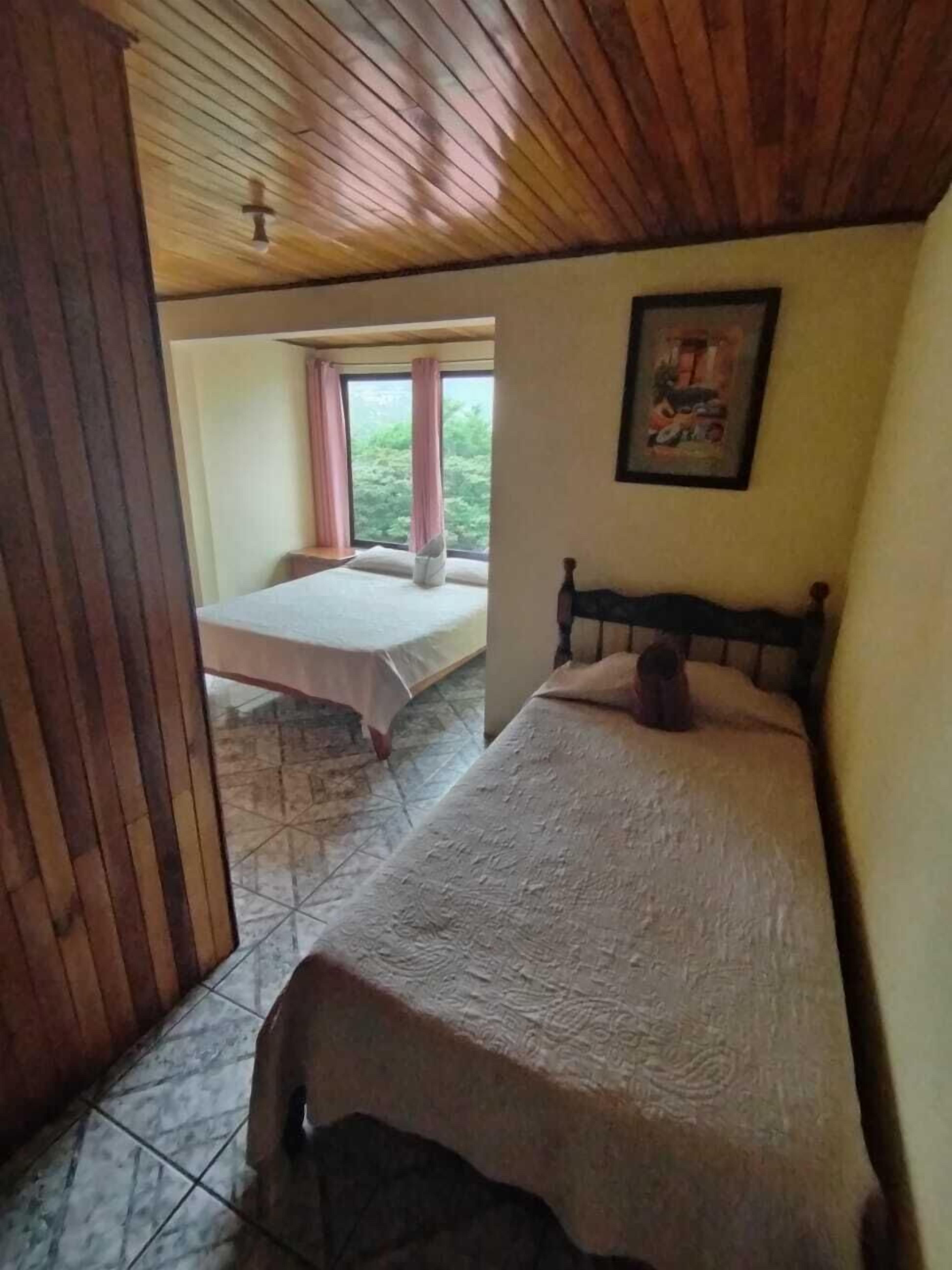 A bedroom with a bed, a window with curtains, and a framed picture on the wall.