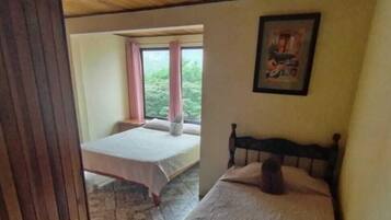 A bedroom with a bed, a window with curtains, and a framed picture on the wall.