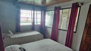 A room with two beds, a wooden ceiling, and a window with curtains. - Monteverde Monkey Hostel (Monteverde)