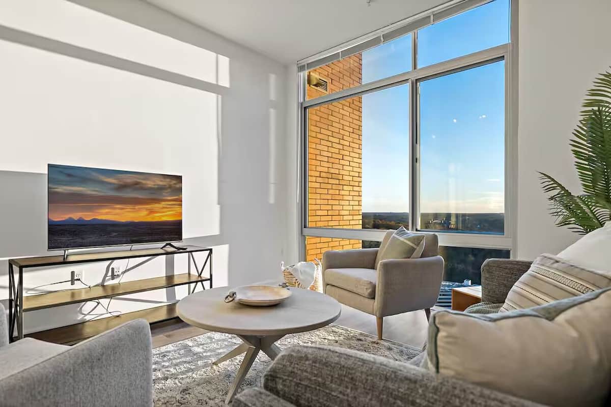 A modern living room with a large window, a flat-screen TV, and comfortable seating.