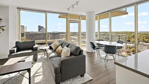 Een moderne woonkamer met een grote bank, een eettafel en stoelen. Grote ramen bieden uitzicht over de stad.