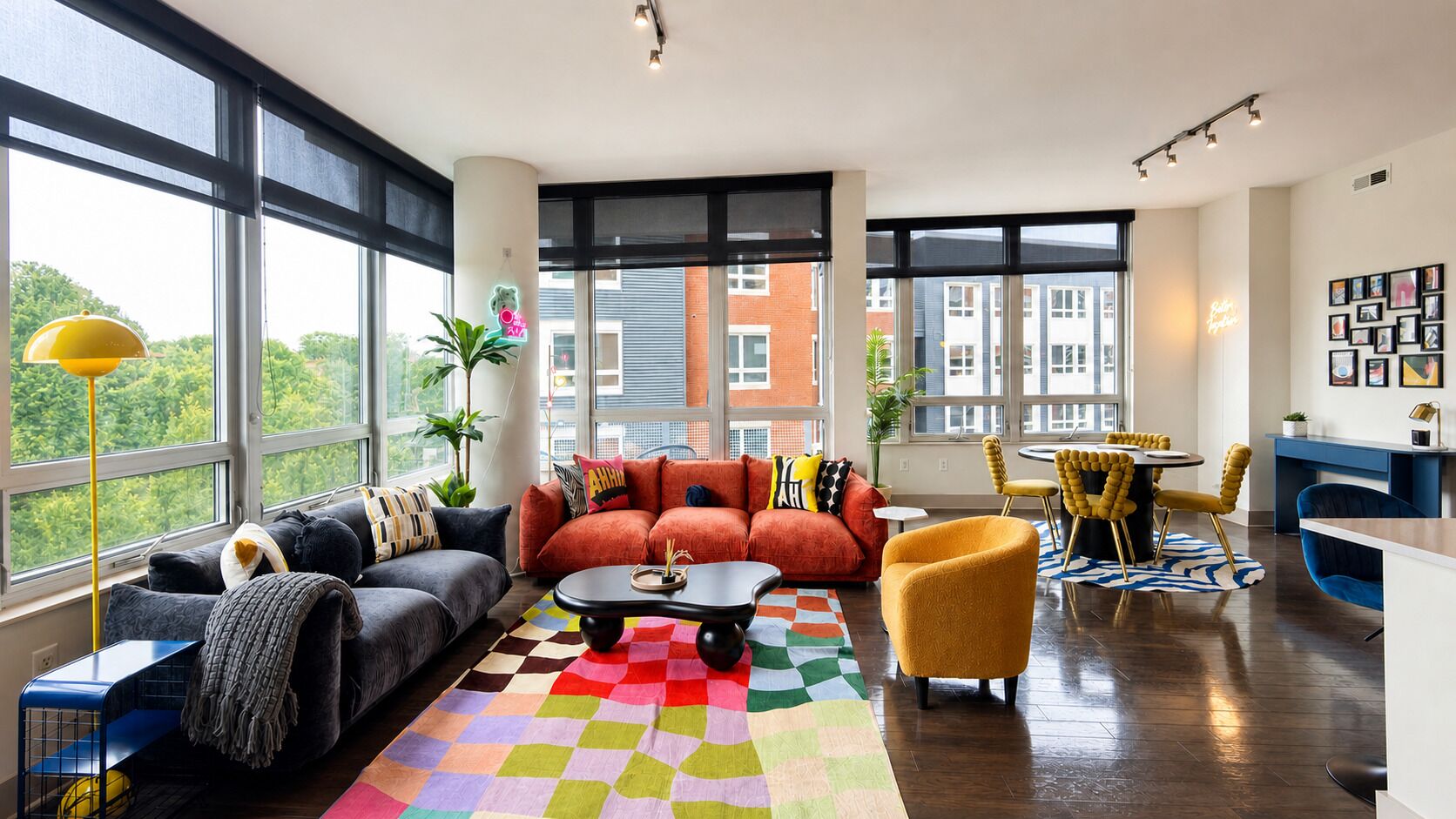 A modern living room with a sofa, coffee table, and chairs, large windows, and a view of buildings.