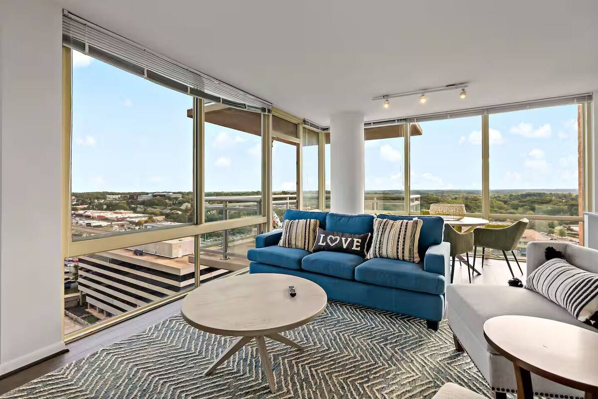 A modern living room with a blue sofa, a round coffee table, and a view of a cityscape through large windows.