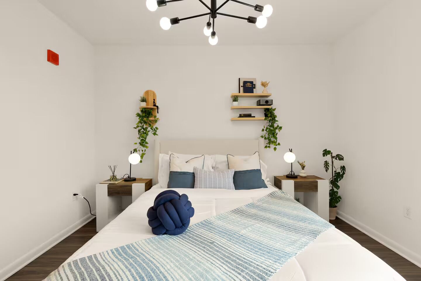 Un dormitori modern amb un llit gran, taules de nit, una planta penjant i un lluminària de sostre.